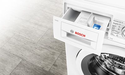 Nahaufnahme eines Waschmaschinen-Fachs mit Reinigungsmitteln, Waschpulver und Weichspüler, bereit für die Wäsche, sauber und ordentlich.